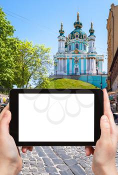 travel concept - tourist photographs Andriyivskyy Descent street and St Andrew's Church in Podil district of Kiev city in Ukraine on tablet with cut out screen for advertising logo