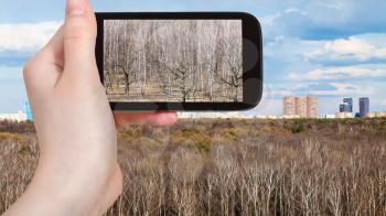 travel concept - tourist photographs Timiryazevskiy urban park and Moscow skyline in Russia in early spring on smartphone
