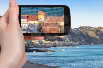 travel concept - tourist photographs residential houses in Giardini Naxos town on coast of Ionian sea in Sicily Italy in summer evening on smartphone