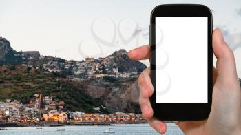 travel concept - tourist photographs Giardini-Naxos town and Taormina city in Sicily Italy in summer evening on smartphone with cut out screen for advertising logo