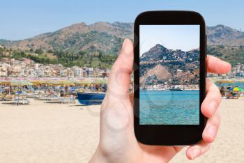 travel concept - tourist photographs Taormina city on cape and in Giardini Naxos town on coast of Ionian sea in Sicily Italy in summer on smartphone