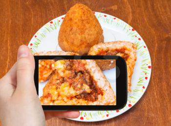travel concept - tourist photographs meat ragu stuffed rice balls arancini on plate (traditional sicilian street food) in Sicily Italy on smartphone