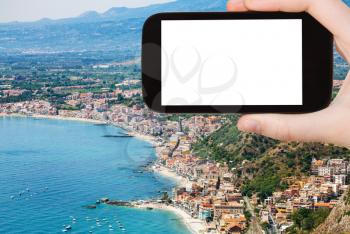 travel concept - tourist photographs Ionian sea shore with Giardini Naxos town in Sicily Italy in summer season on smartphone with cut out screen for advertising logo