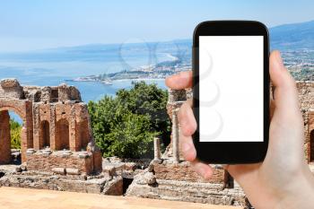 travel concept - tourist photographs ruined ancient Greek Theater (Teatro Greco) in Taormina city in Sicily Italy in summer on smartphone with cut out screen for advertising logo