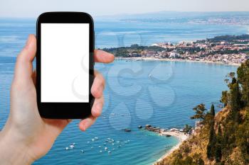 travel concept - tourist photographs Ionian sea coastline with Giardini Naxos town in Sicily Italy in summer season on smartphone with cut out screen for advertising logo