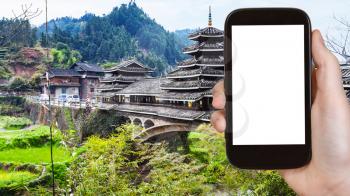 travel concept - tourist photographs Wind and Rain (Fengyu) bridge in Chengyang village of Sanjiang Dong Autonomous County in China on smartphone with cut out screen for advertising logo