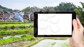 travel concept - tourist photographs rice fields near irrigation canal in Chengyang village of Sanjiang Dong Autonomous County in China in spring on tablet with cut out screen for advertising logo