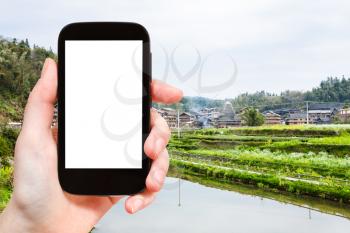 travel concept - tourist photographs terraced field near irrigation canal in Chengyang village of Sanjiang Dong Autonomous County in China in spring on smartphone with cut out screen for advertising