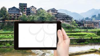 travel concept - tourist photographs country houses and terraced gardens near irrigation canal in Chengyang village of Sanjiang Dong Autonomous County in China on tablet with cut out screen