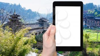 travel concept - tourist photographs Wind and Rain (Fengyu) bridge in Chengyang village of Sanjiang Dong Autonomous County in China in spring on tablet with cut out screen for advertising