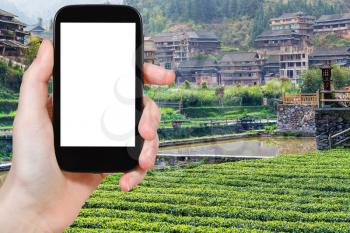 travel concept - tourist photographs tea plantation near irrigation canal in Chengyang village of Sanjiang Dong Autonomous County in China in spring on smartphone with cut out screen for advertising
