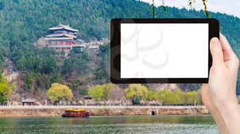 travel concept - tourist photographs pagodas on East Hill of Chinese Buddhist monument Longmen Caves (Dragon's Gate Grottoes) through Yi river on tablet with cut out screen for advertising logo