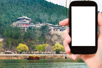 travel concept - tourist photographs temples on East Hill of Chinese Buddhist monument Longmen Caves (Dragon's Gate Grottoes) through Yi river on smartphone with cut out screen for advertising logo