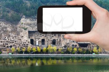 travel concept - tourist photographs Caves on West Hill of Chinese Buddhist monument Longmen Grottoes (Dragon's Gate) on bank of Yi River on smartphone with cut out screen for advertising logo