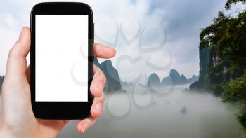 travel concept - tourist photograps fog over river near Xingping town in Yangshuo county in China in spring morning on smartphone with cut out screen for advertising logo