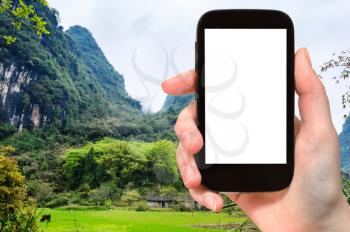 travel concept - tourist photographs green field near karst mountain in Yangshuo County in China in spring season on smartphone with cut out screen for advertising logo