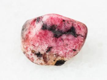 macro shooting of natural mineral rock specimen - polished pink rhodonite gem stone on white marble background from Ural mountains in Russia