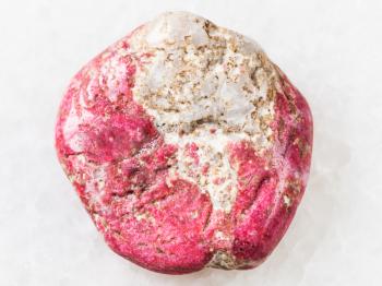 macro shooting of natural mineral rock specimen - tumbled Thulite gemstone on white marble background from Leksvik, Norway
