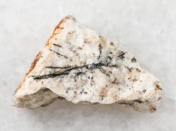 macro shooting of natural mineral rock specimen - black Ludwigite crystals in rough stone on white marble background from Praskovie-Evgenyevskaya mine, South Ural, Russia