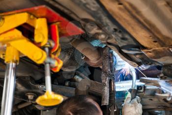 repairing of corrugation muffler of exhaust system in car workshop - worker welds the silencer on car by argon welding