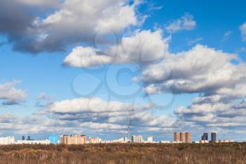 white clouds in blue sky over woods in Timiryazevskiy park and skyline of Moscow city in sunny spring day