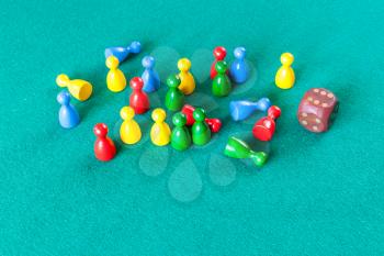 wooden dice and multicolored board game pawns on green baize table