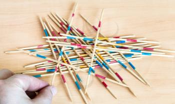 player picks up a stick from pile in Mikado pick-up sticks game on wood board