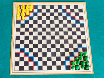 setup for two player on checkered gameboard of Halma strategy board game on green baize table. Halma board game was invented by George Howard Monks in1883-1884