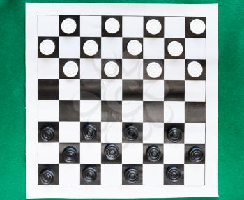 top view of draughts on black and white checkered sheet board on green baize table