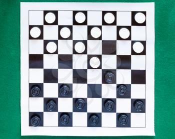 top view of checkers on black and white checkered sheet board on green baize table