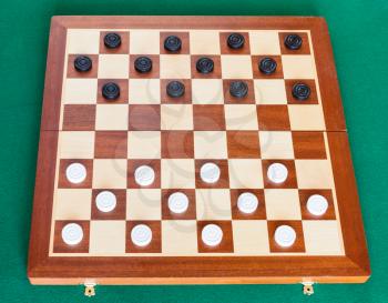 draughts on wooden checkered board on green baize table