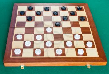 checkers on wooden checkered board on green baize table