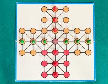 top view of cross solitaire board game on green baize table. The first mention of peg solitaire game can be identified in France in 1697