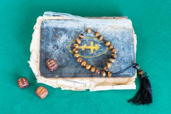 old psalm book, worry beads and three wooden dices with six points on green baize table