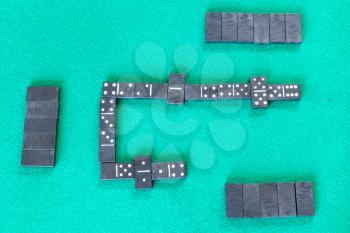 top view of gameplay of dominoes board game with black tiles on green baize table