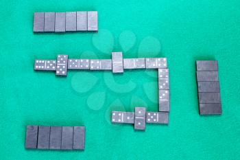 top view of playfield of dominoes board game with black tiles on green baize table