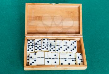 set of white dominoes tiles in bamboo box on green baize table