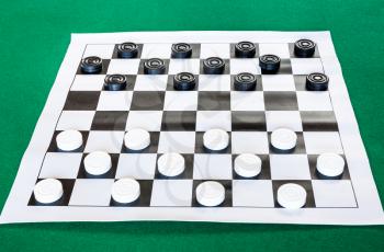 draughts on black and white checkered sheet board on green baize table