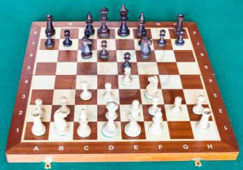 view from white side of chess gameplay on wooden chessboard on green baize table