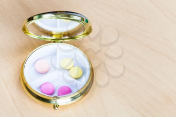 open pillbox with pink and yellow pills on wooden board