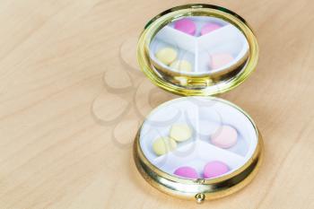 open pillbox with mirror with pink and yellow pills on wooden board