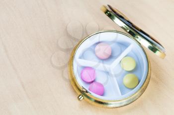 top view of pillbox with pink and yellow pills on wooden board