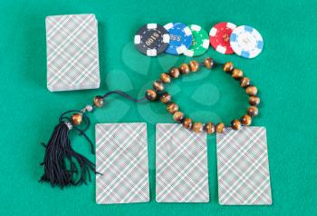 top view of card decks, casino tokens and worry beads on green baize table