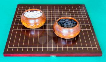 white and black playing stones for Go game in bowls on wooden board on green table