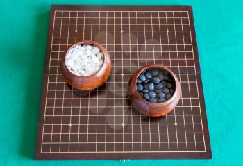 top view of white and black playing stones for Go game in bowls on wooden board on green table