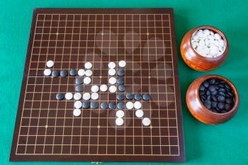 top view of gameplay of Go game and playing stones in bowls and wooden board on green table