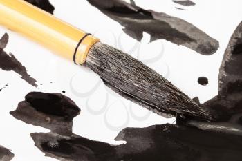 black dyed round goat hair tip of bamboo paintbrush for sumi-e ( suibokuga) painting over ink spots on white paper close up