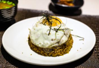 korean cuisine - Kimchi bokkeum bap (fried rice with kimchi, beef and fried egg) on white plate on brown leathed board in local restaurant