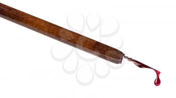 side view of red ink drop dripping from tip of nib of brown dip pen close up isolated on white background