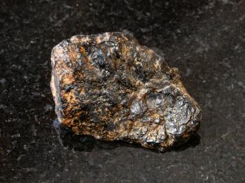 macro shooting of natural rock specimen - rough Cassiterite (Tin ore) stone on black granite background from Pravourmiyskoe deposit in Khabarovsk Krai, Russia